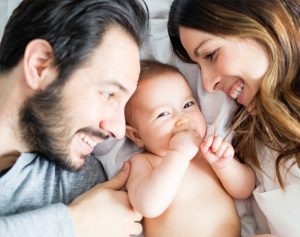 Ein Vater und eine Mutter liegen mit ihrem Baby gemeinsam im Bett.