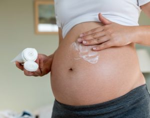 Eine Frau cremt ihren schwangeren Bauch ein.