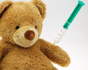 Ein Kuschelbär mit Spritze im Arm wird geimpft.
