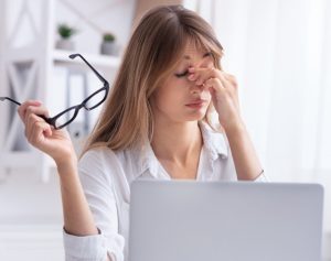 Junge Frau sitzt vor ihrem Laptop und reibt sich müde die Augen.