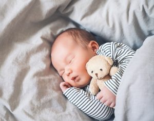 Ein schlafendes Baby umarmt einen kleinen Kuschelbären.