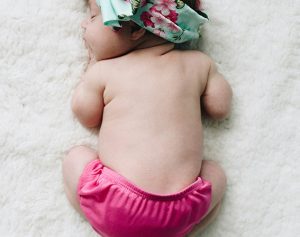 Ein Baby in einer rosa Unterhose liegt auf einer weißen Decke.