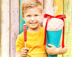 Eine Junge hält einen Lolli und eine Schultüte in der Hand und lächelt.