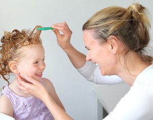 Eine Mutter kämmt ihrem Kind mit dem Flohkamm durch die eingeschäumten Haare.