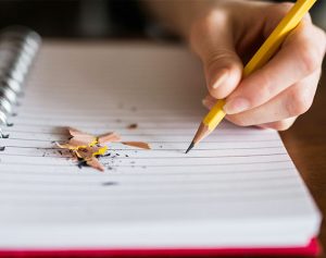 Ein Kind schreibt mit einem Bleistift etwas in einen Block.