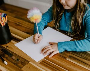 Mädchen sitzt am Schreibtisch und schreibt etwas auf ein Blatt Papier.