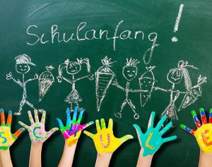 Bunt bemalte Kinderhände mit Buchstaben in den Handflächen, die das Wort ‚Schule‘ ergeben.