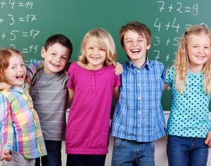 Lachende Schulkinder, die vor einer Schultafel stehen.