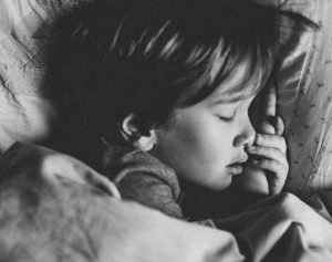 Ein schwarz weiß Bild auf dem ein Kleinkind im Bett liegt und schläft.