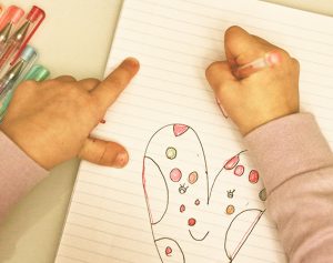 Kind zeichnet mit einem Stift rote Herzen in sein Heft.