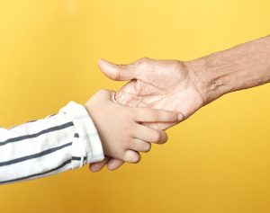 Eine Kinderhand und die Hand einer älteren Person geben einander die Hand.